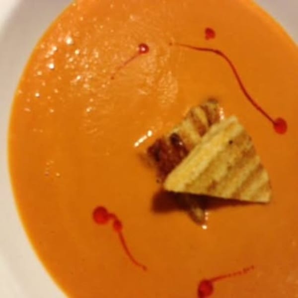 Close-up of creamy orange soup with grilled croutons and red oil drizzle.