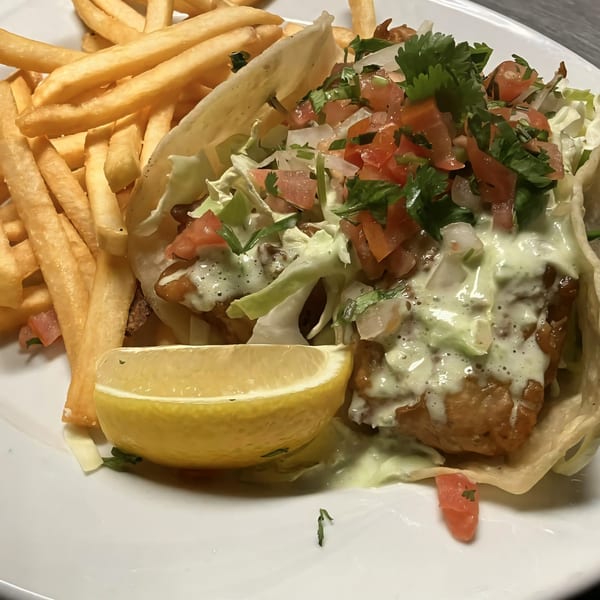 Two fish tacos topped with salsa, lettuce, and crema, served with french fries and a lemon wedge.