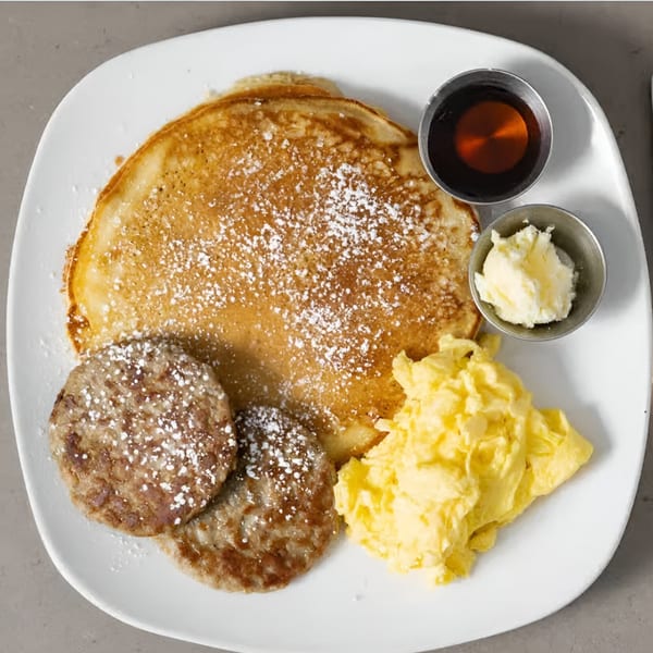 Sienna & Hope breakfast plate with pancakes, sausage patties, scrambled eggs, syrup, and butter.