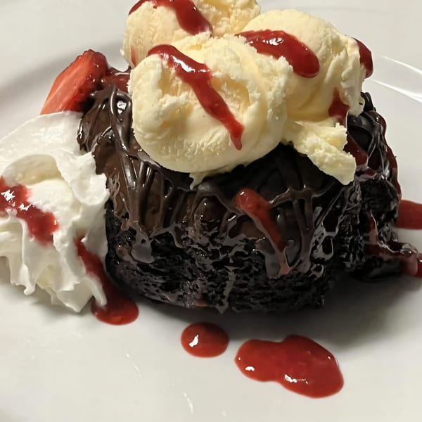 Chocolate lava cake topped with vanilla ice cream, strawberry sauce, whipped cream, and a strawberry slice.